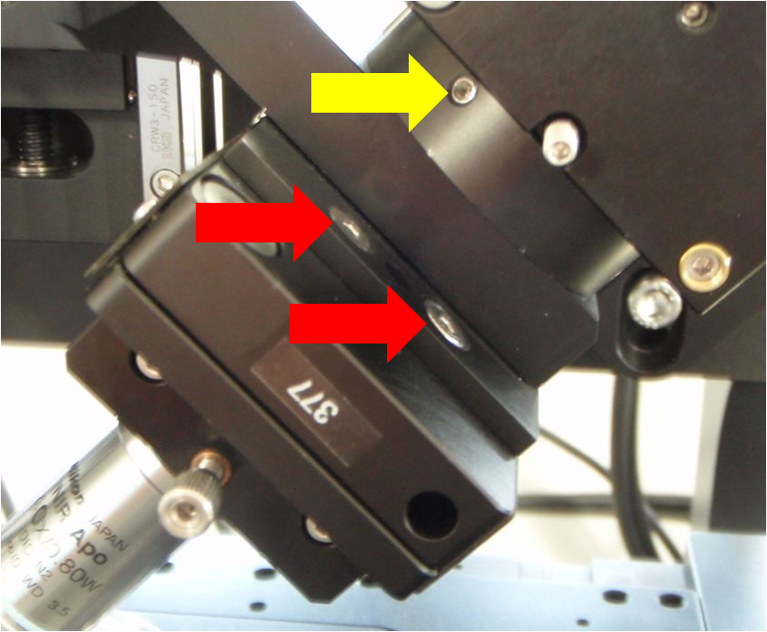 Close-up view of the screws holding the lower cube and rest of SPIM arm to the arm mount (yellow arrow) and also the screws holding the piezo objective mover to the SPIM arm mount (red arrows)